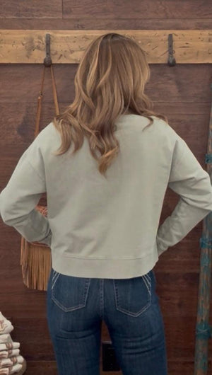 Person wearing a light-colored sweatshirt and blue jeans standing in front of a wooden wall with hooks.
