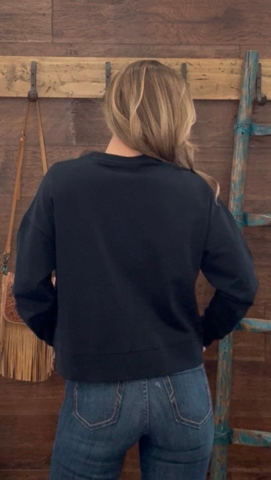 Person wearing a black sweatshirt and blue jeans standing in front of a wooden wall with a broom and ladder.