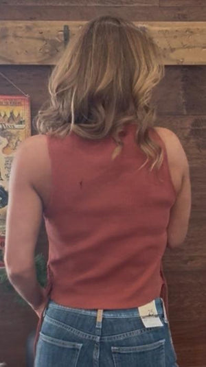 Person wearing a red tank top and blue jeans standing in front of a wooden wall with posters.