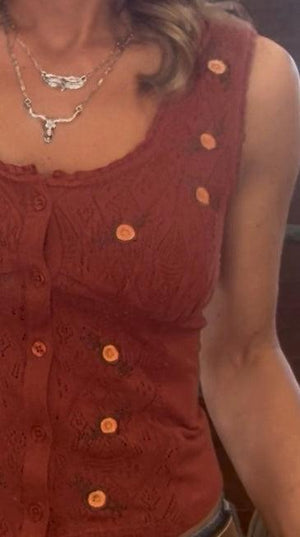 Close-up of a person wearing a rust-colored sleeveless top with orange buttons.