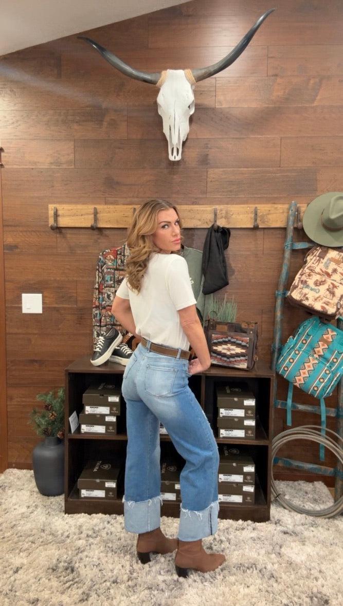 Person wearing blue jeans standing in front of a wooden shelf.