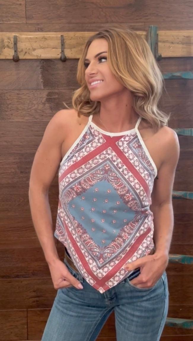 Woman wearing a patterned halter top and jeans against a wooden background