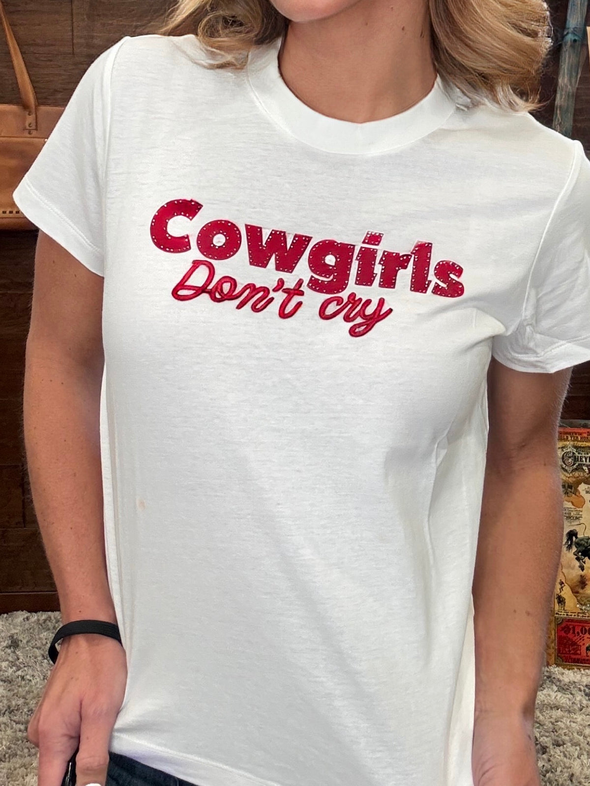 A woman wearing a white crewneck t-shirt with 'Cowgirls Don't cry' printed in red across the chest, shown in a close-up shot.