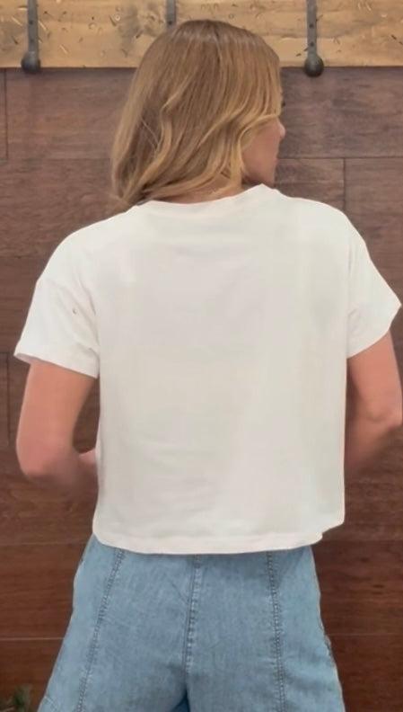 Person wearing a white t-shirt and blue jeans standing against a wooden wall.