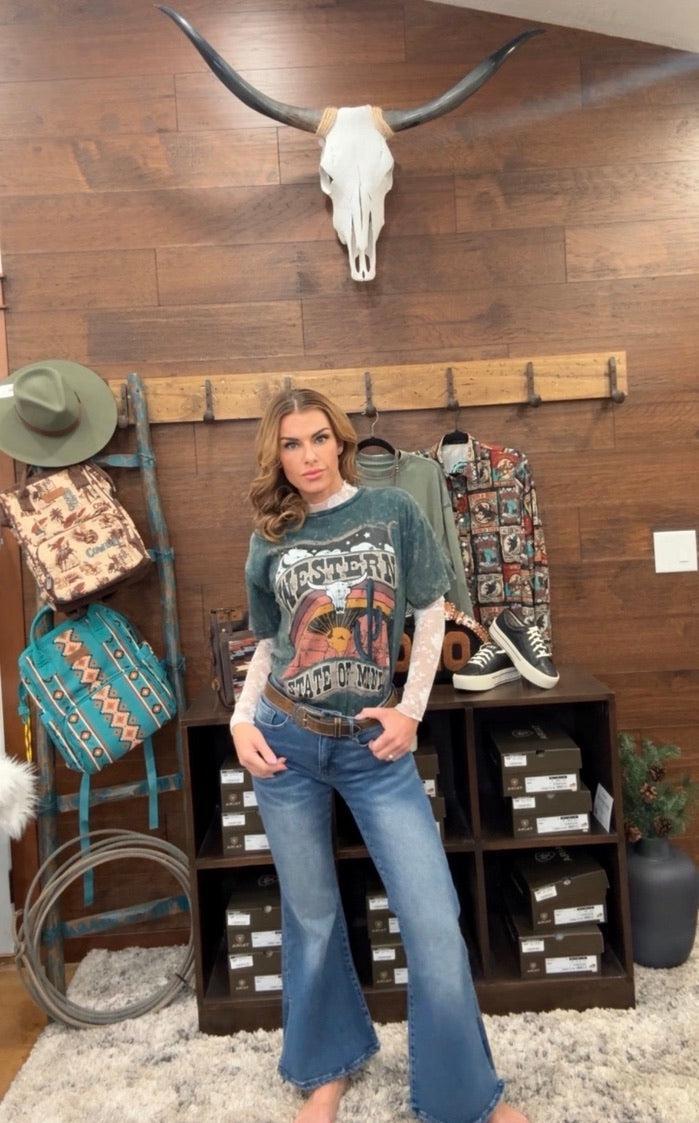 Woman in a store wearing a graphic t-shirt and jeans, with a cow skull and decor on the wall.