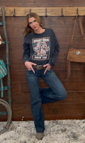 Woman wearing a graphic sweatshirt and jeans standing against a wooden wall