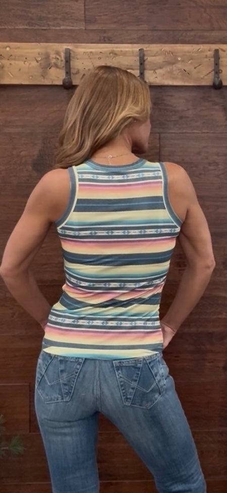 Person wearing a striped tank top and jeans against a wooden wall.