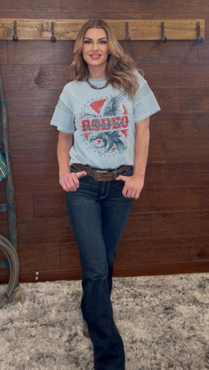 Woman wearing a graphic t-shirt and jeans standing against a wooden wall.