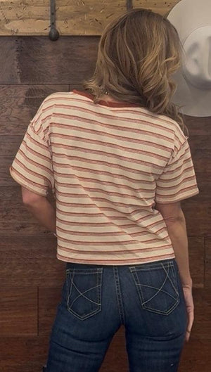 Person wearing a striped shirt and jeans standing against a wooden wall.