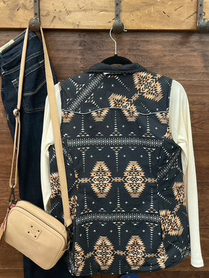 A sleeveless patterned vest with a black base and beige geometric Southwestern-style motifs, layered over a cream long-sleeve shirt