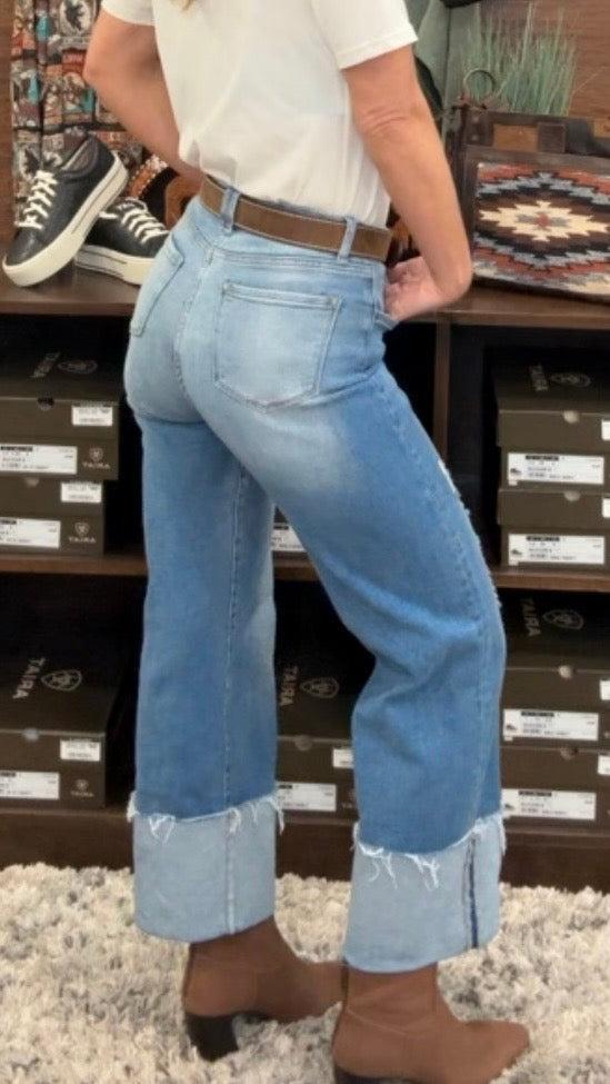 Person wearing blue jeans standing in front of a wooden shelf.