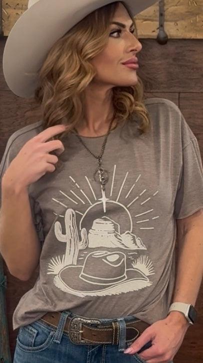Woman wearing a gray t-shirt with a graphic design, sitting against a wooden wall.