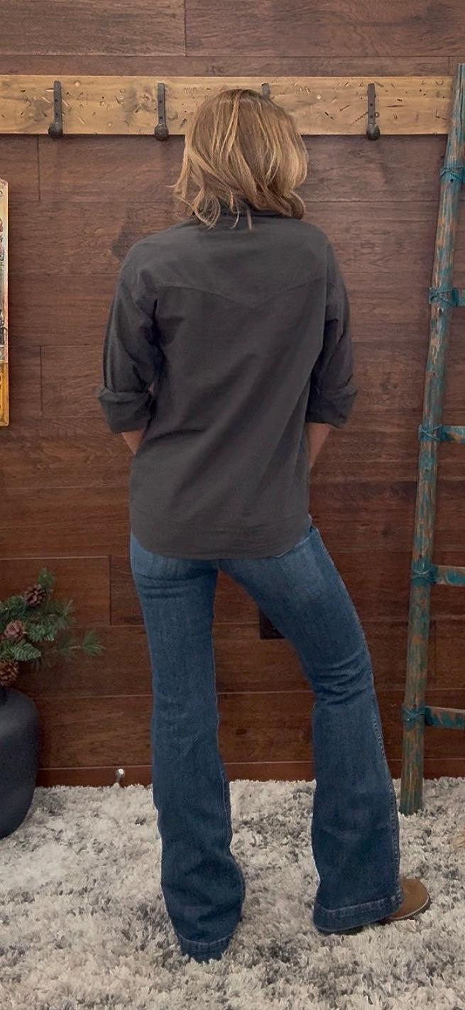 Person wearing a gray shirt and blue jeans standing in front of a wooden wall with a ladder.