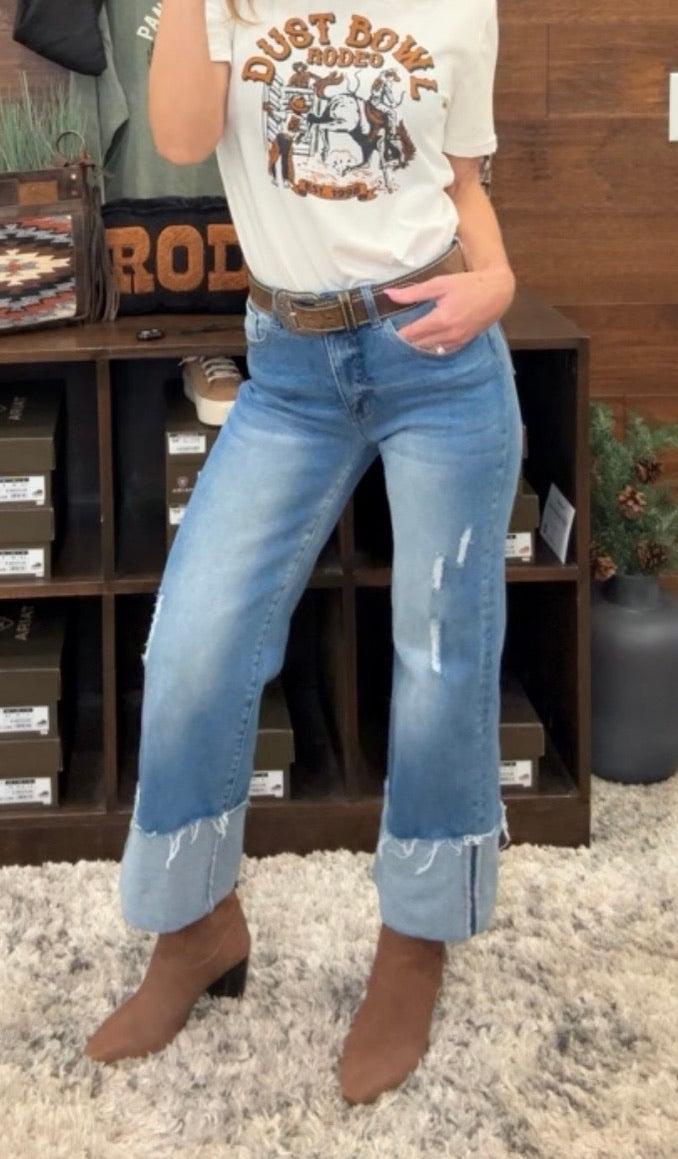 Person wearing blue jeans standing in front of a wooden shelf.