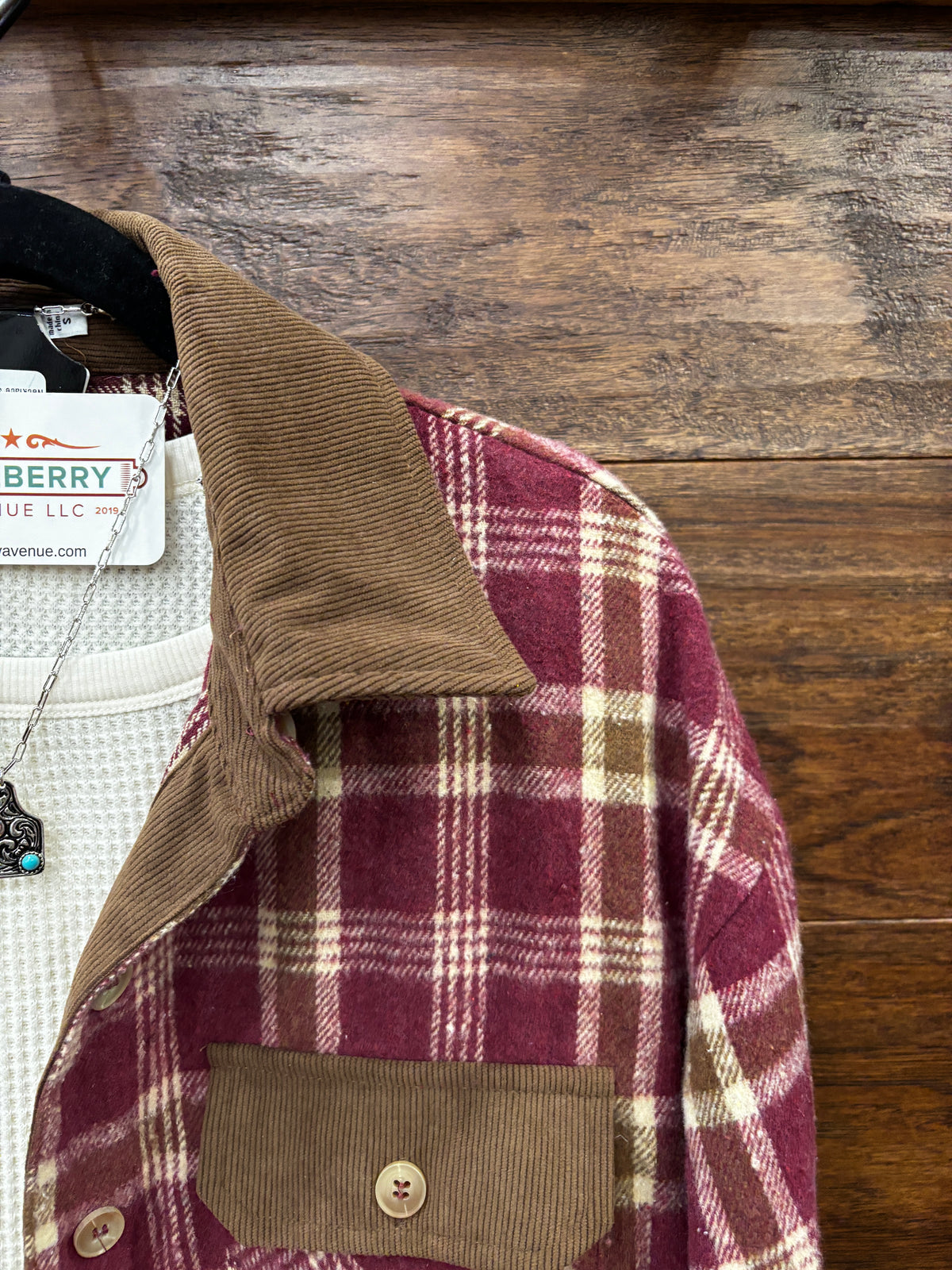 A burgundy and beige plaid flannel shirt with a brown corduroy collar and chest pockets