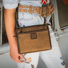 Person holding a brown leather bag with decorative strap in front of a vintage van.