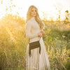 Woman in a long dress standing in a field of tall grass and wildflowers with a warm, golden light.