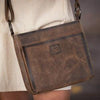 Brown leather bag with a visible brand logo worn by a person.