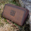Brown leather pouch with a brand logo on grass and rocks