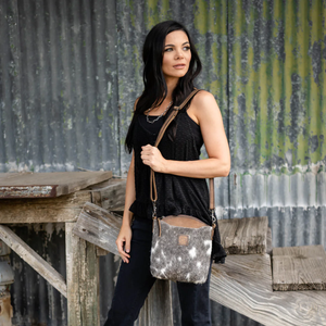 Woman holding a cowhide bag against a rustic metal wall.