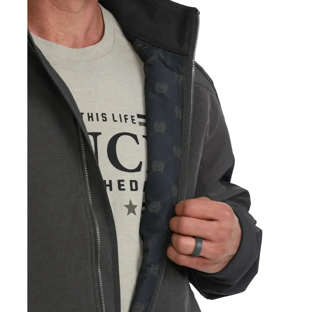 A man wearing a dark gray and black Clinch outdoor jacket with a full-zip front, zippered chest pocket, and vertical Clinch branding on the sleeve, paired with blue jeans against a white background.