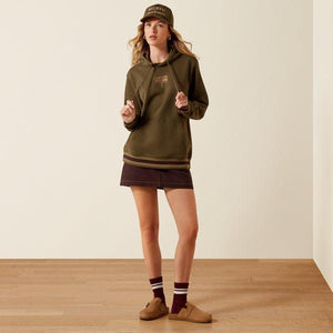 A woman wearing an olive green pullover hoodie with drawstrings, a kangaroo pocket, and ribbed cuffs and hem with thin tan stripes.
