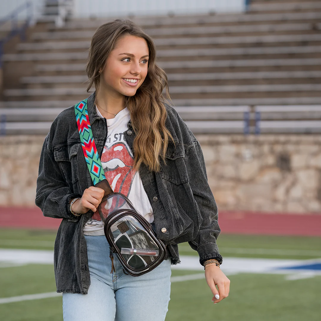 Woman holding a clear bag with a colorful strap on a sports field