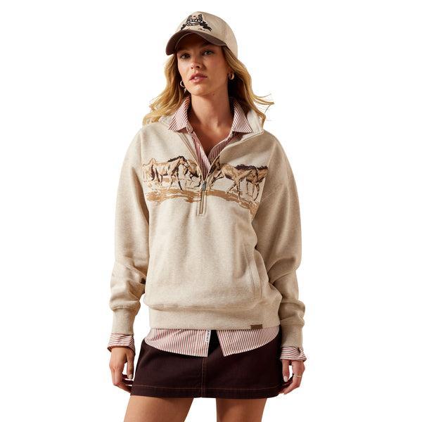 Woman wearing a beige half-zip sweatshirt with graphic designs on a white background