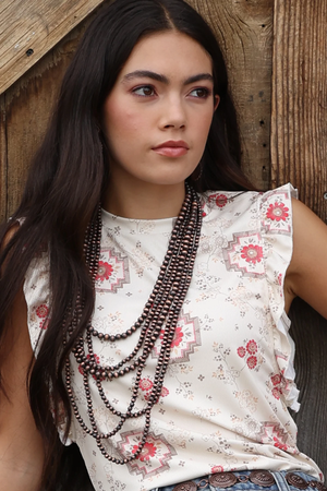 Woman wearing a floral top and layered necklaces against a wooden background