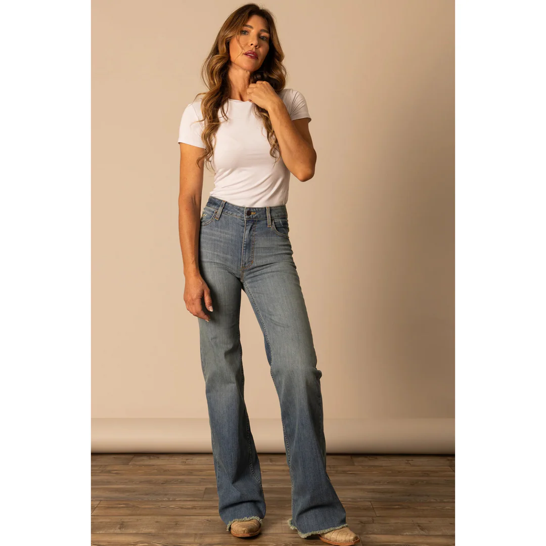 Woman wearing a white t-shirt and blue jeans against a beige wall.