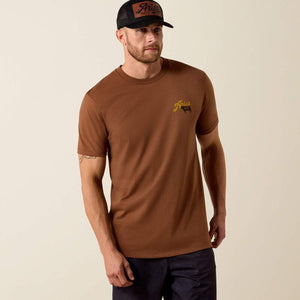 Man wearing a brown Ariat t-shirt with yellow text and a cow graphic on the back.