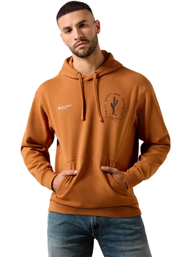A man wearing a burnt orange pullover hoodie with a drawstring hood and kangaroo pocket, featuring a black circular cactus graphic on the left chest and a small white logo on the right chest, paired with blue jeans against a plain white background.