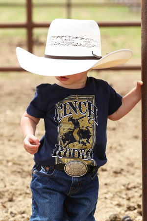Child wearing a navy blue shirt with a graphic design and a white cowboy hat, standing in an outdoor setting.