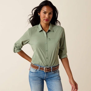 Woman wearing a green shirt and blue jeans against a beige background