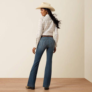 Woman wearing a white blouse, blue jeans, and a beige cowboy hat on a plain background