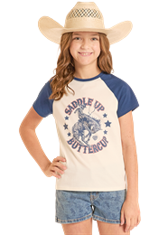 Young girl wearing a cowboy hat and a t-shirt with a graphic design, standing against a plain background.