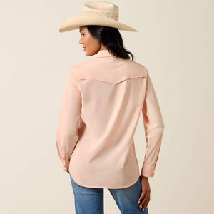 Woman wearing a light peach shirt and blue jeans with a beige hat on a beige background