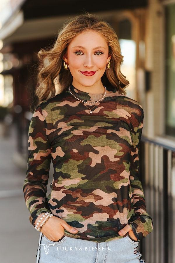 Woman wearing a camouflage long-sleeve top with 'Lucky & Blessed' branding.