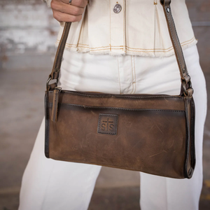 Brown leather handbag held by a person wearing a white jacket and pants.
