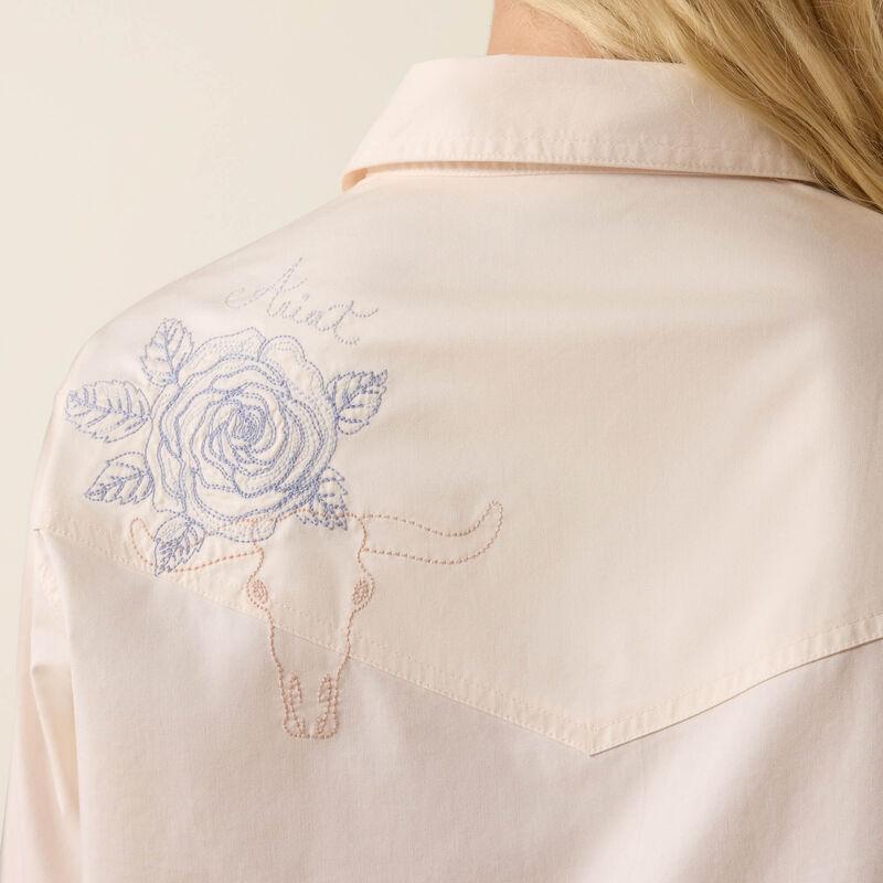 Close-up of a beige shirt with blue floral embroidery on the back.