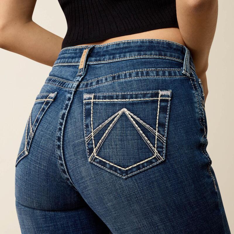 Close-up back view of a person wearing blue denim jeans with contrast white stitching and a black ribbed crop top against a light beige studio background.