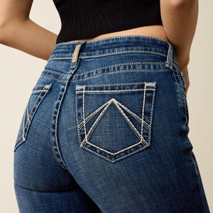 Close-up back view of a person wearing blue denim jeans with contrast white stitching and a black ribbed crop top against a light beige studio background.