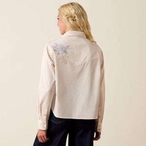 Woman wearing a beige shirt with floral embroidery on a plain background