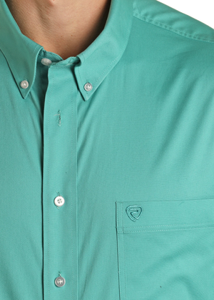Close-up of a teal button-up shirt with a brand logo on the chest pocket.
