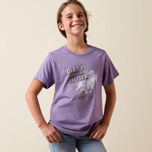 Young girl wearing a purple t-shirt with 'Dirt is Cowgirl Glitter' text and graphic on a beige background