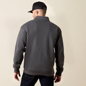 A man wearing a dark gray quarter-zip sweatshirt, shown from the back, paired with a black baseball cap and dark jeans, against a plain beige studio background.
