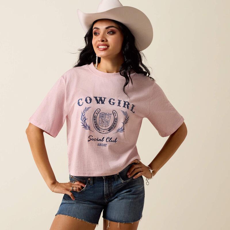 Woman wearing a pink 'Cowgirl Social Club' t-shirt with a cowboy hat on a beige background
