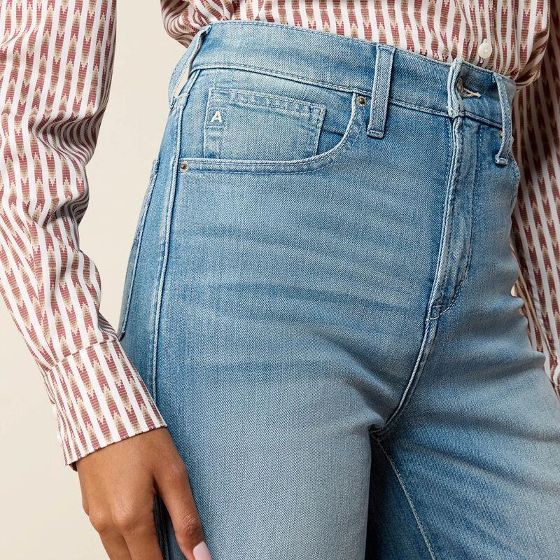 Close-up of a person wearing light blue denim jeans with a red and white patterned shirt, showing the front pocket and waistband details.