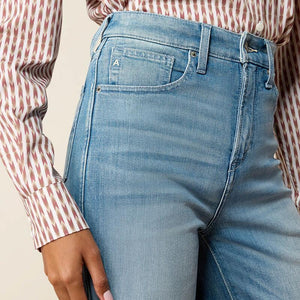 Close-up of a person wearing light blue denim jeans with a red and white patterned shirt, showing the front pocket and waistband details.