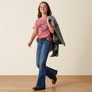 Young girl wearing a pink shirt, blue jeans, and brown boots holding a denim jacket.